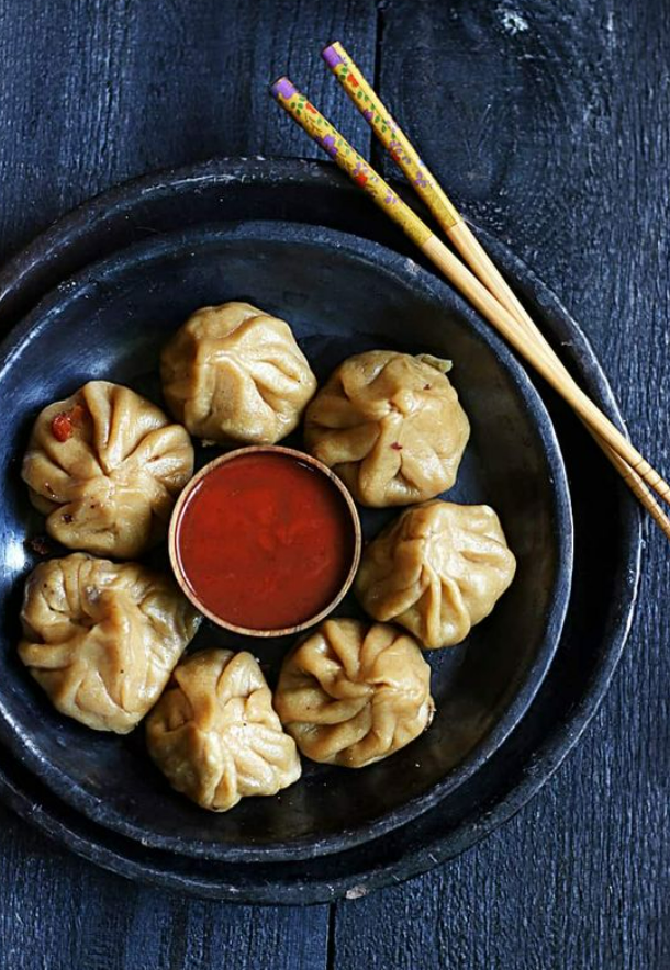 A plate of 6 momos paired with red chili and garlic chutney, served with chopsticks