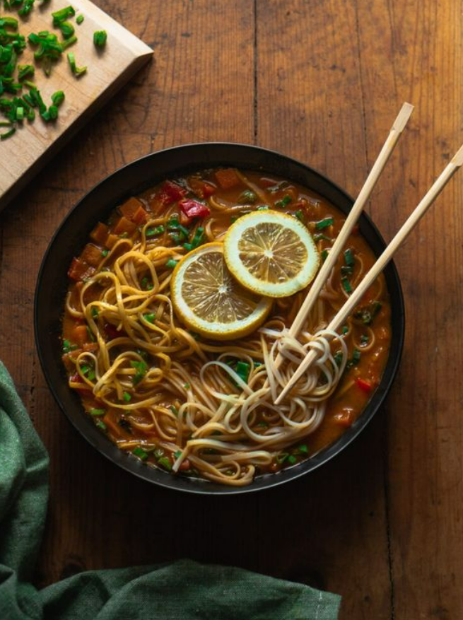 Bowl of thukpa garnished with lemon slices and spring onions and served with chopsticks
