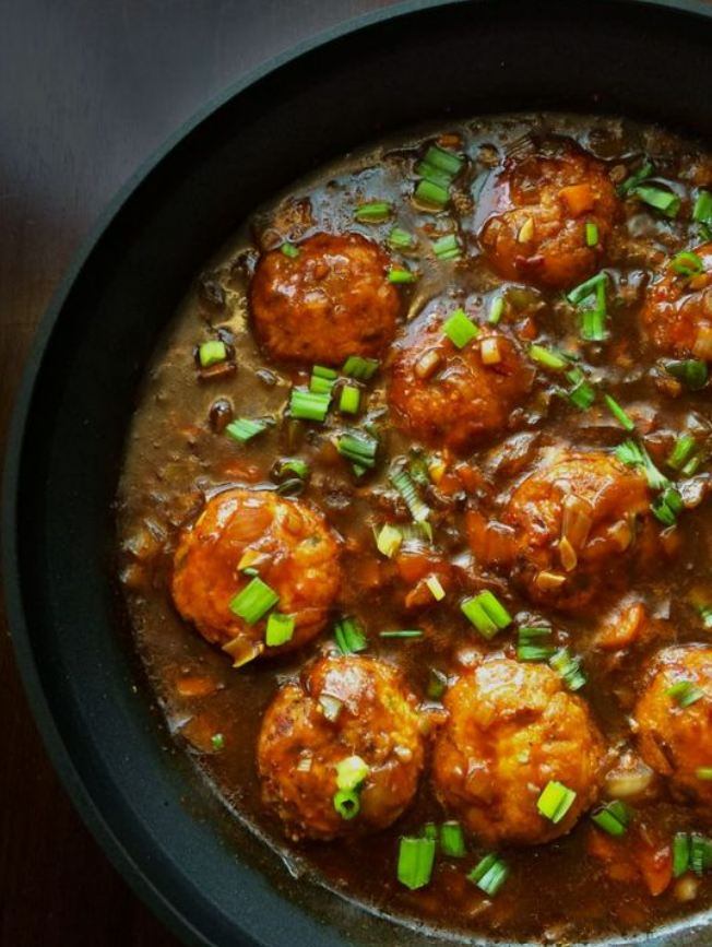 Bowl of manchurian balls dipped in soy sauce and garnished with spring onions